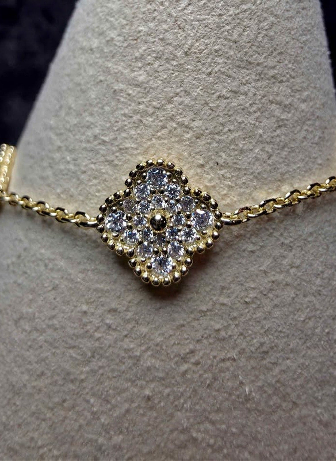A gold chain bracelet with a central diamond cluster charm, displayed on a textured light gray jewelry cone.