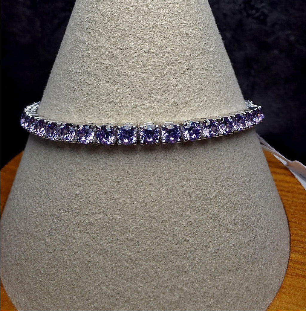 A silver tennis bracelet with rectangular purple gemstones, displayed on a textured beige jewelry cone stand.