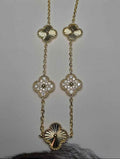 A gold-toned necklace with four clover-shaped pendants, each adorned with small clear stones, displayed on a light gray surface.